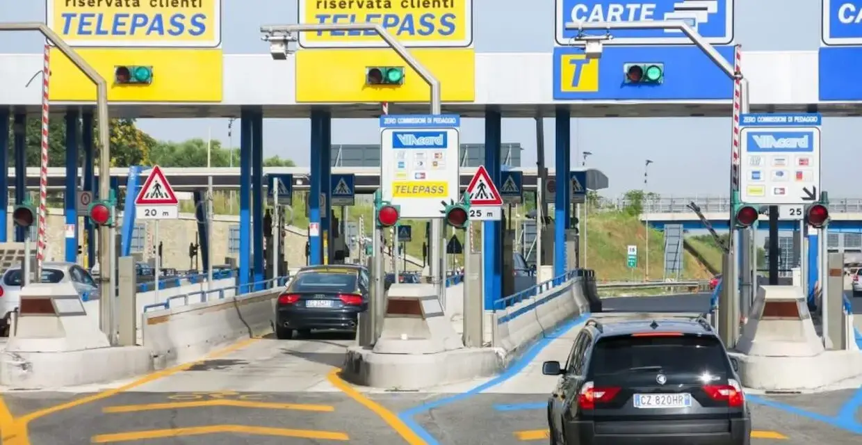 Casello autostradale con corsie Telepass e carte. Un'auto nera si avvicina, sperando che il suo Telepass non funzioni per evitare una multa.