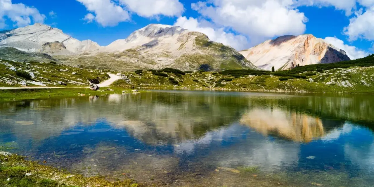 Un limpido lago di limo riflette montagne maestose e un cielo azzurro con nuvole bianche.