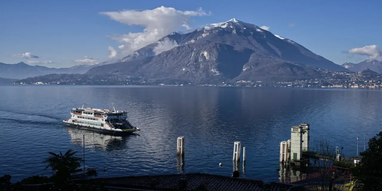 Traghetto sul lago di Como, con montagne innevate sullo sfondo e il pittoresco varenna centro storico.