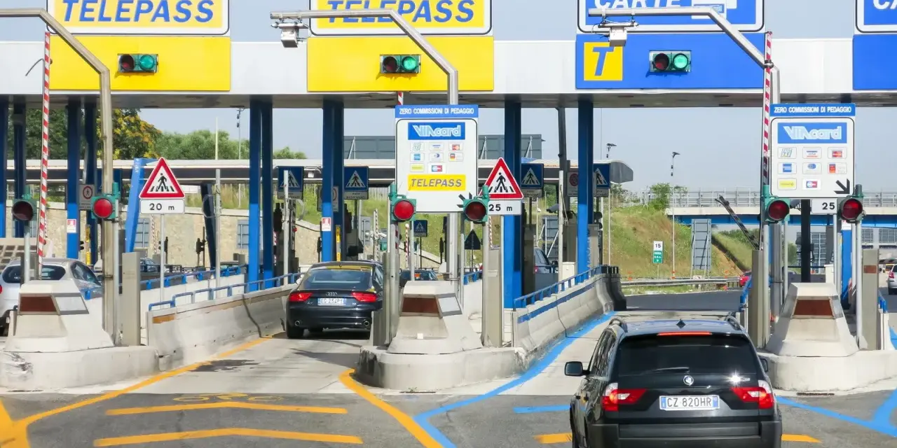 Casello autostradale con auto in coda. Segnaletica per Telepass e carte di credito. Possibile problema di mancato pagamento Telepass per un veicolo.