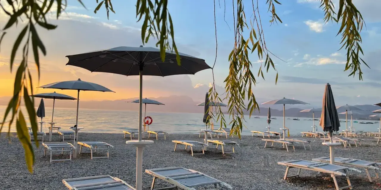 Alba sul lago di Garda, con lettini e ombrelloni pronti per accogliere i bagnanti sulle sue spiagge di sabbia.