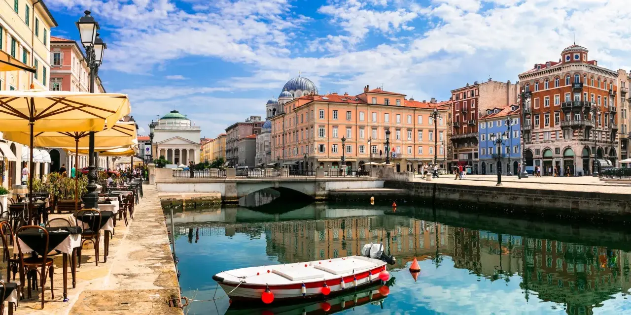 Un'incantevole vista di Trieste: un canale con una barca, caffè all'aperto e palazzi storici. Ecco cosa vedere a Trieste per un'esperienza indimenticabile.