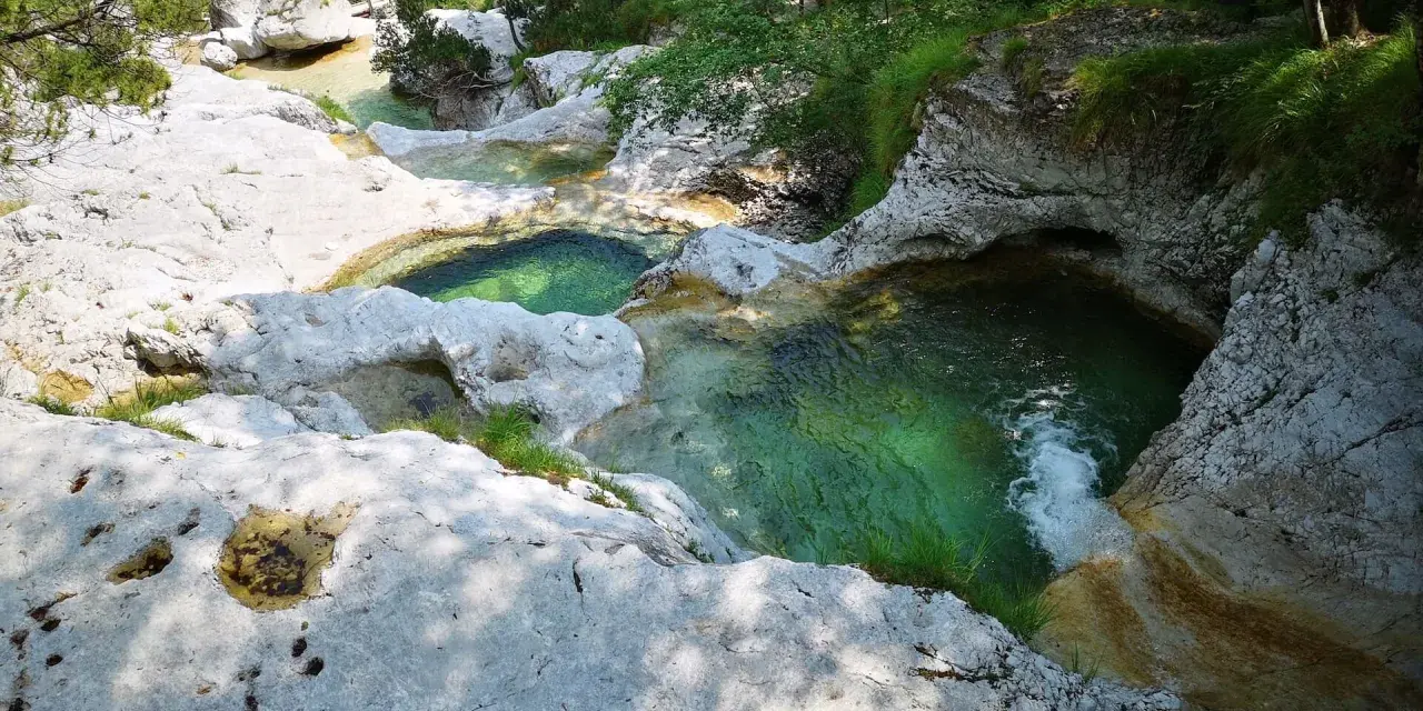 Acque cristalline scorrono tra le rocce levigate dei **cadini del Brenton**, creando piscine naturali immerse nel verde.