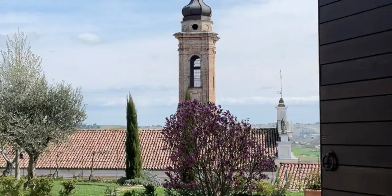 Torre campanaria e un albero in fiore, scorcio di un borgo tra le colline. Castagnole delle Lanze cosa vedere: un paesaggio incantevole.