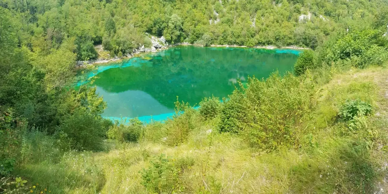Lago di origine carsica a Forgaria nel Friuli, con acque cristalline di un verde smeraldo intenso, circondato da vegetazione lussureggiante.