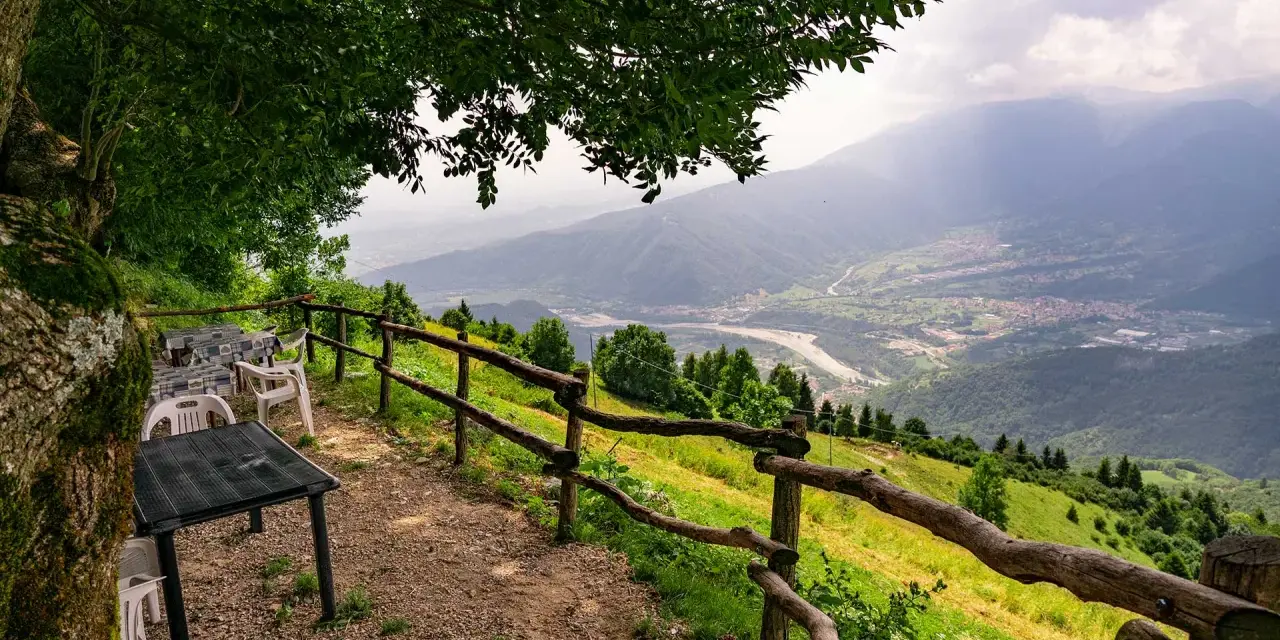 Tavoli e sedie sotto un albero offrono una vista panoramica sulla valle dalla malga Molvine Binot.