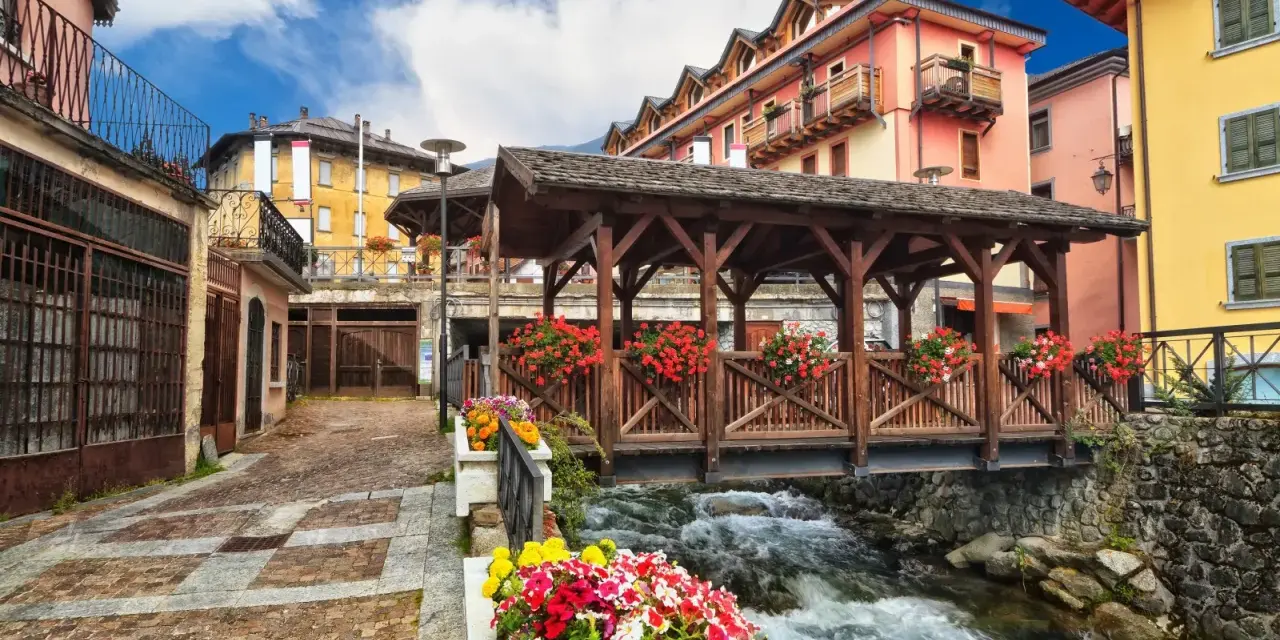 Un pittoresco ponte di legno coperto, adornato di fiori, attraversa un torrente impetuoso. Un incantevole scorcio di cosa vedere in un borgo alpino.