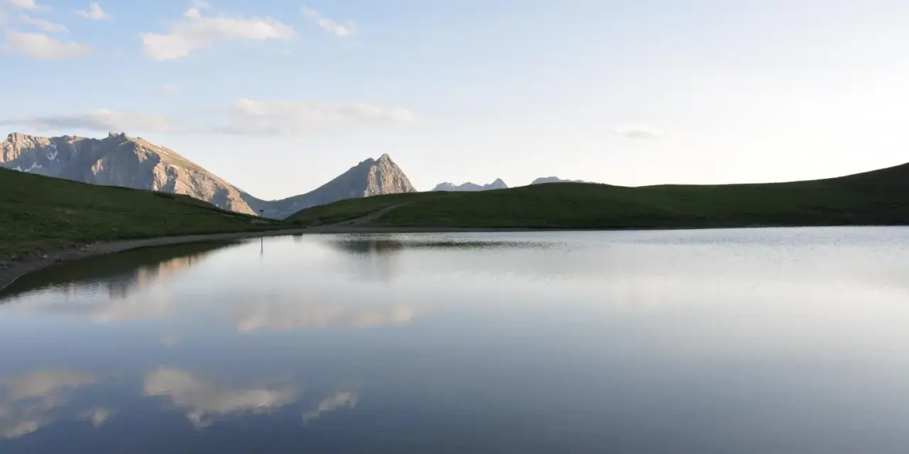 Sestriere estate: un lago alpino riflette le montagne e il cielo azzurro, un'oasi di pace.