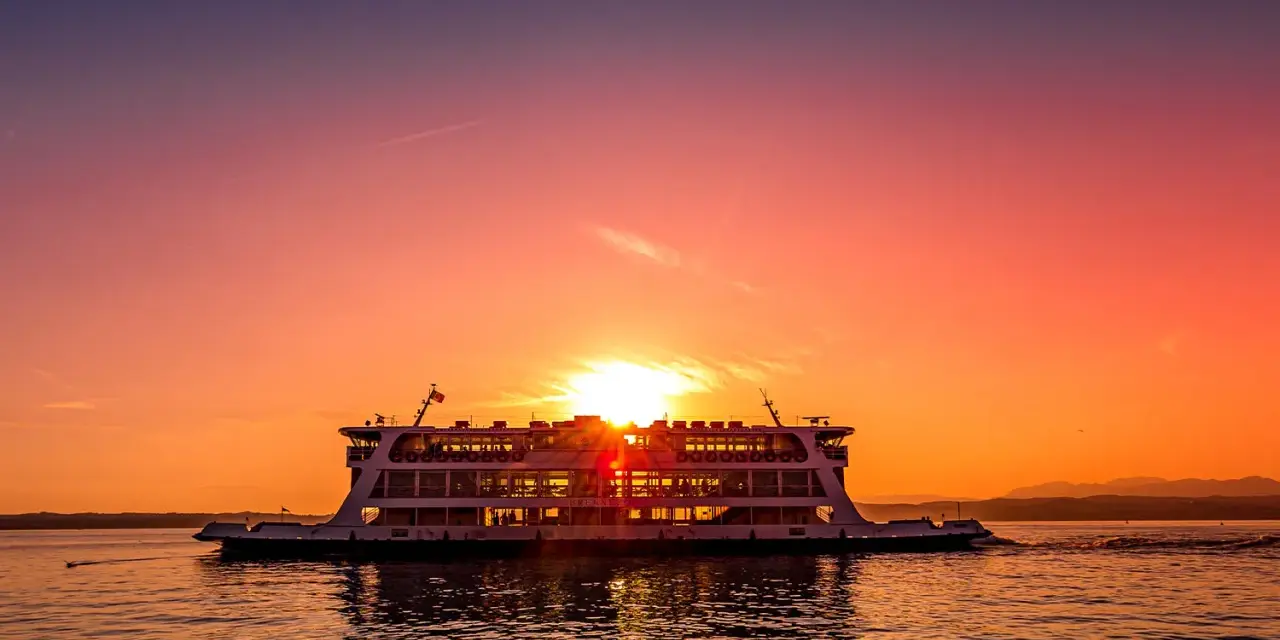 Traghetto in navigazione sul Lago di Garda al tramonto, con il sole che illumina il cielo e il riflesso sull'acqua.