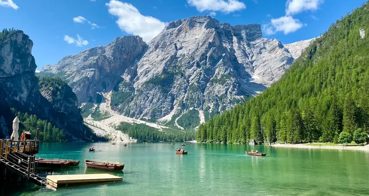 Barche sul **Pragser Wildsee** con montagne imponenti e foreste verdi.