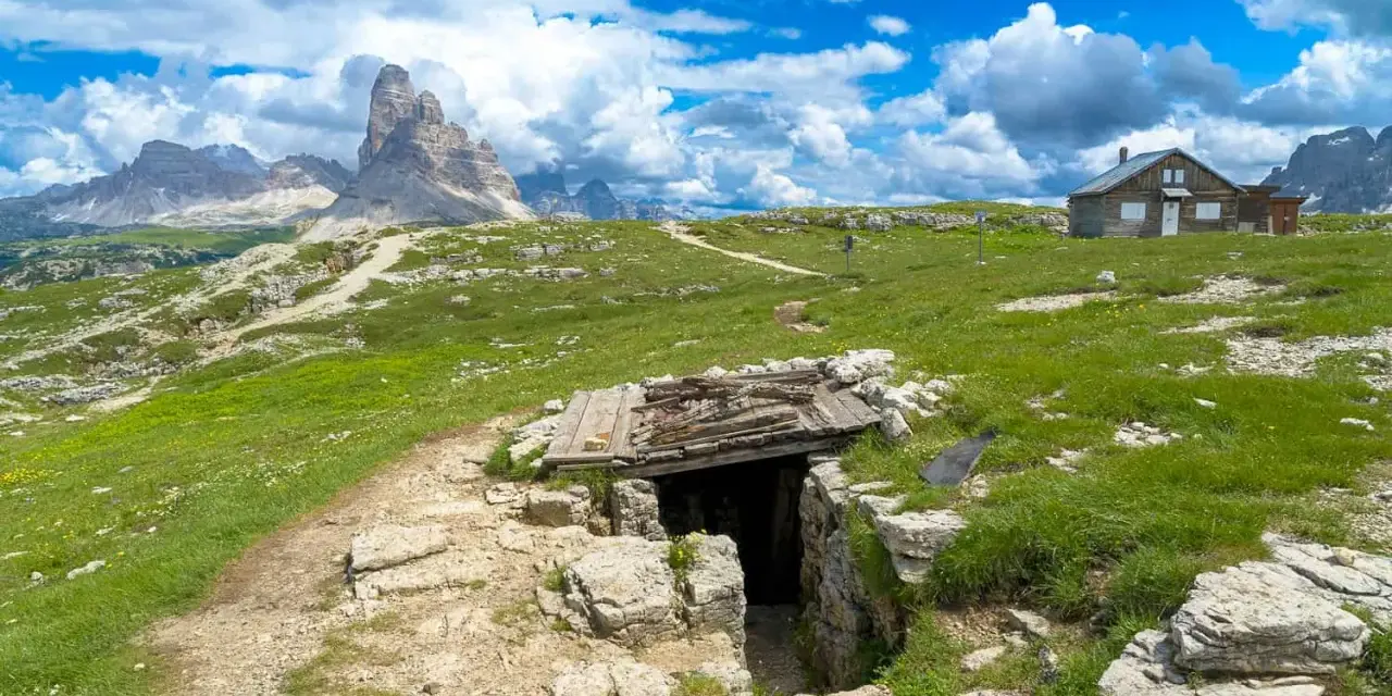Un sentiero conduce a un rifugio di guerra sul Monte Piana, con le maestose Tre Cime di Lavaredo sullo sfondo.