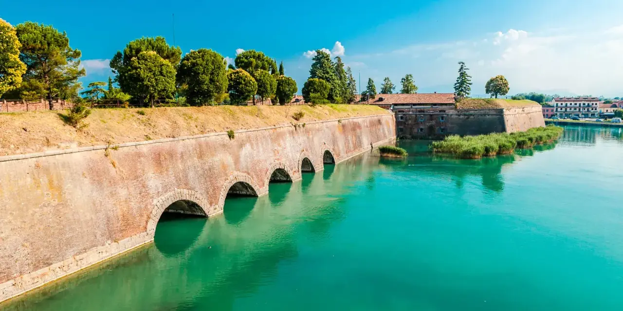 Fortificazioni storiche con archi in mattoni e acqua turchese, dove si trova Peschiera del Garda.