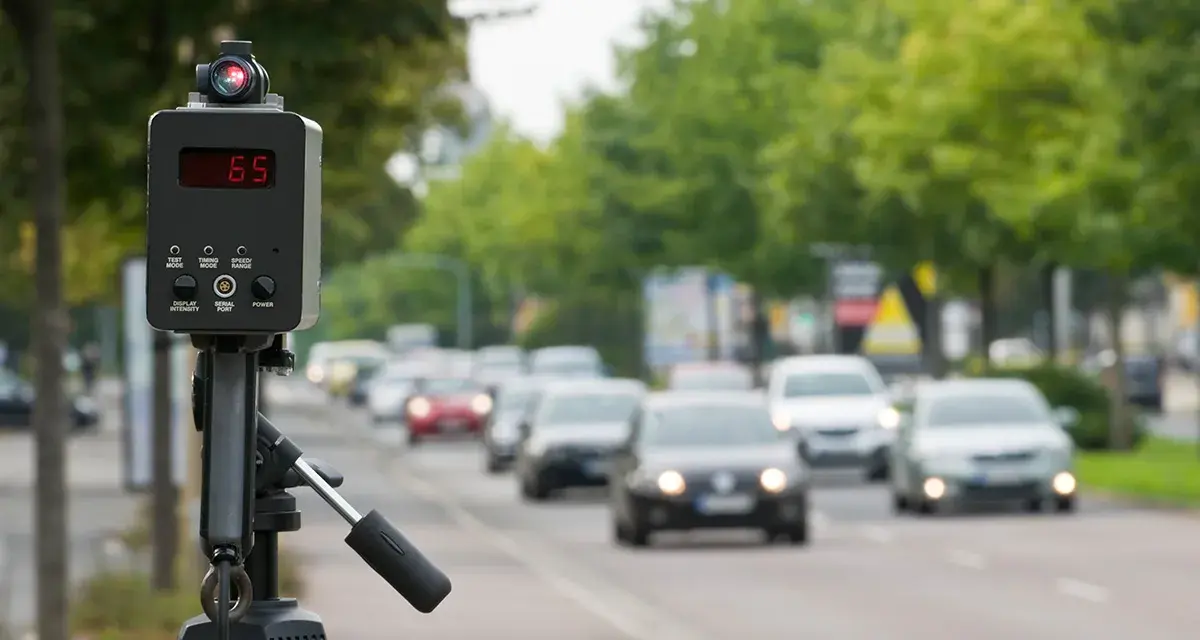 Autovelox mobile come funziona: un dispositivo su treppiede misura la velocità delle auto in transito su una strada alberata.