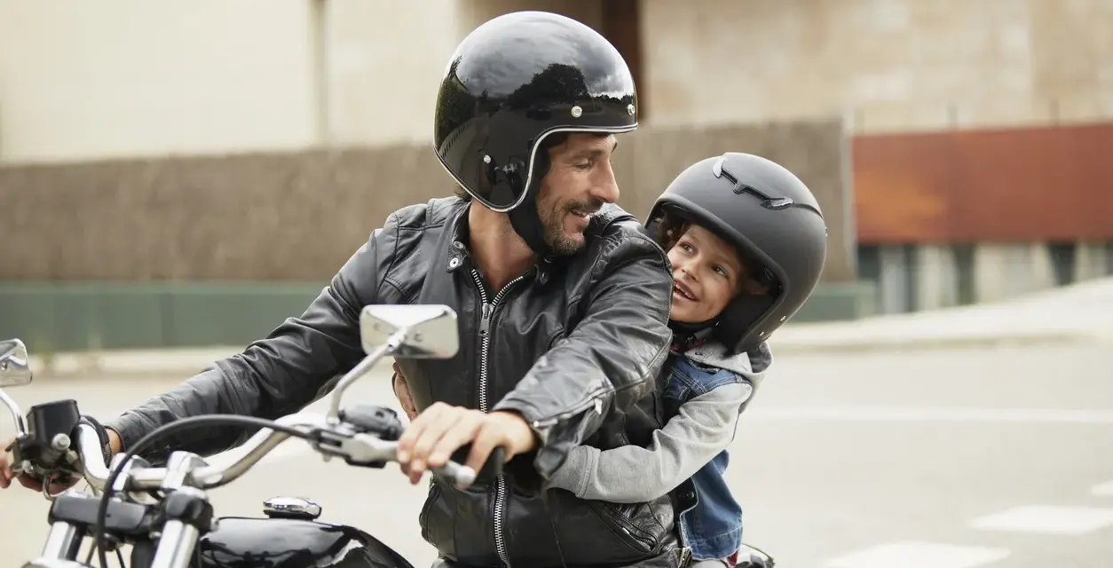 Padre e figlio sorridono in moto, rispettando il nuovo codice della strada per bambini in moto.