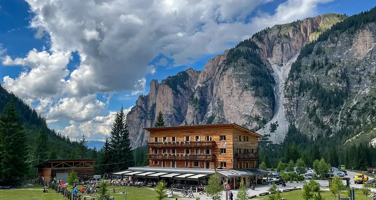 Edificio in legno a Pederu San Vigilio, con montagne imponenti e cielo nuvoloso.