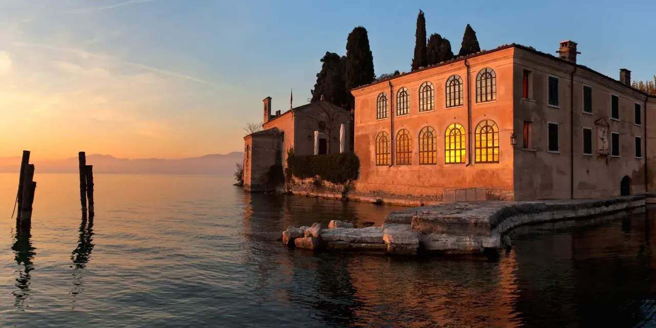 Punta San Vigilio: un tramonto dorato illumina la spiaggia e l'antica villa affacciata sul lago.