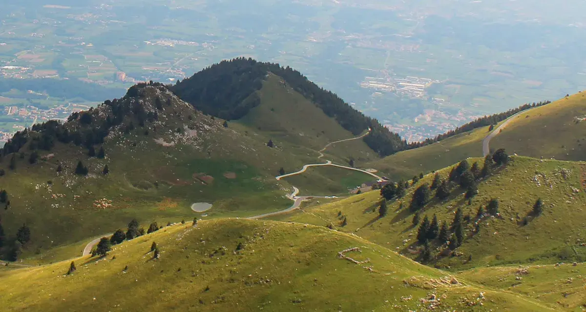 Panorami verdi con strade tortuose e malghe sul Monte Grappa. Un gregge pascola vicino a un piccolo lago.