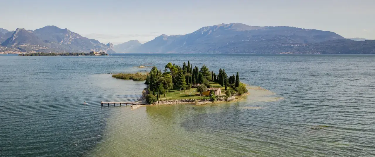 Un'incantevole isola dei conigli sul Lago di Garda, con un piccolo molo e una casetta gialla tra i cipressi.