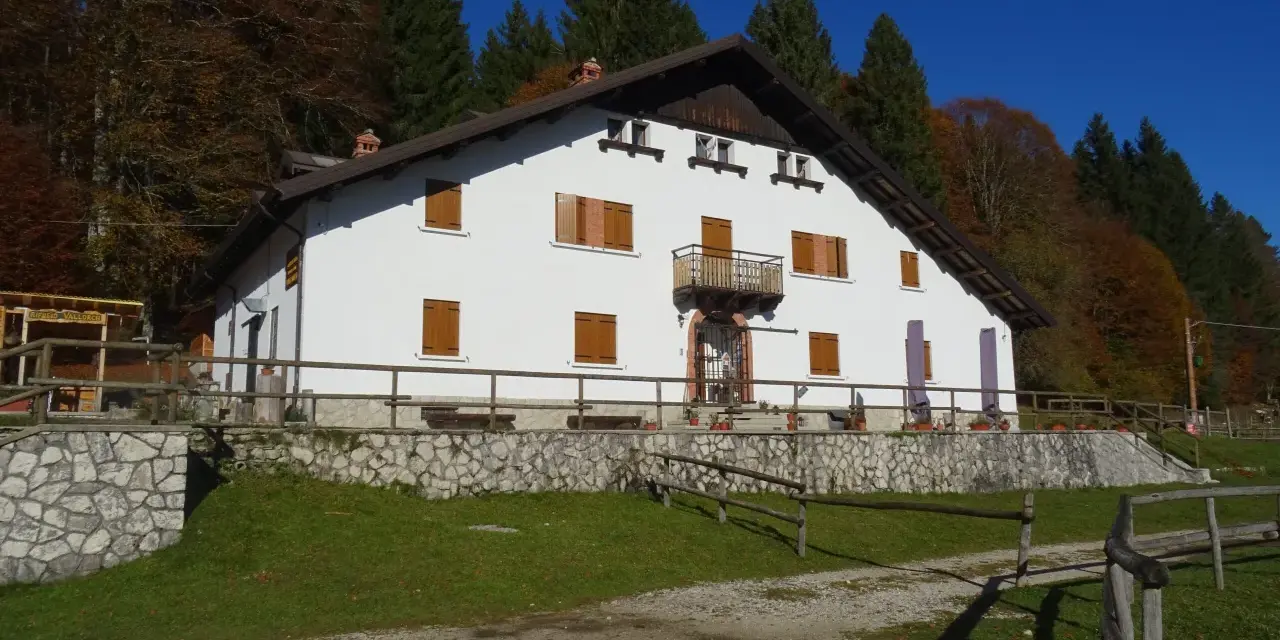 Il rifugio Città di Vittorio Veneto, immerso nel foliage autunnale, accoglie con la sua facciata bianca e le finestre con persiane in legno.