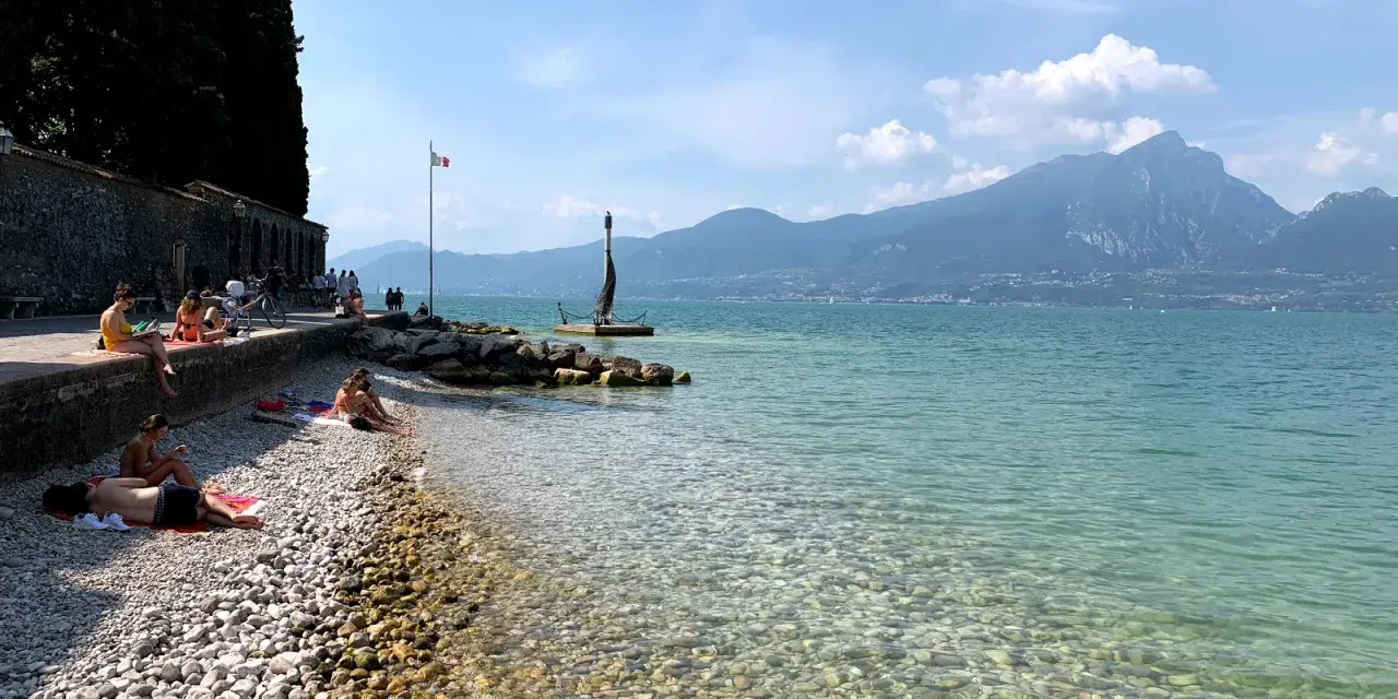 Persone rilassate sulla torri del benaco spiaggia, con acque limpide e montagne sullo sfondo.
