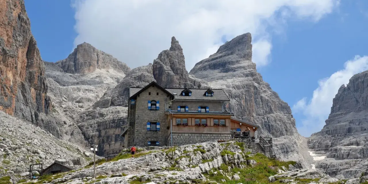 Il rifugio Tuckett e Sella, un'oasi di pietra tra le imponenti vette dolomitiche, accoglie escursionisti sotto un cielo azzurro e nuvoloso.