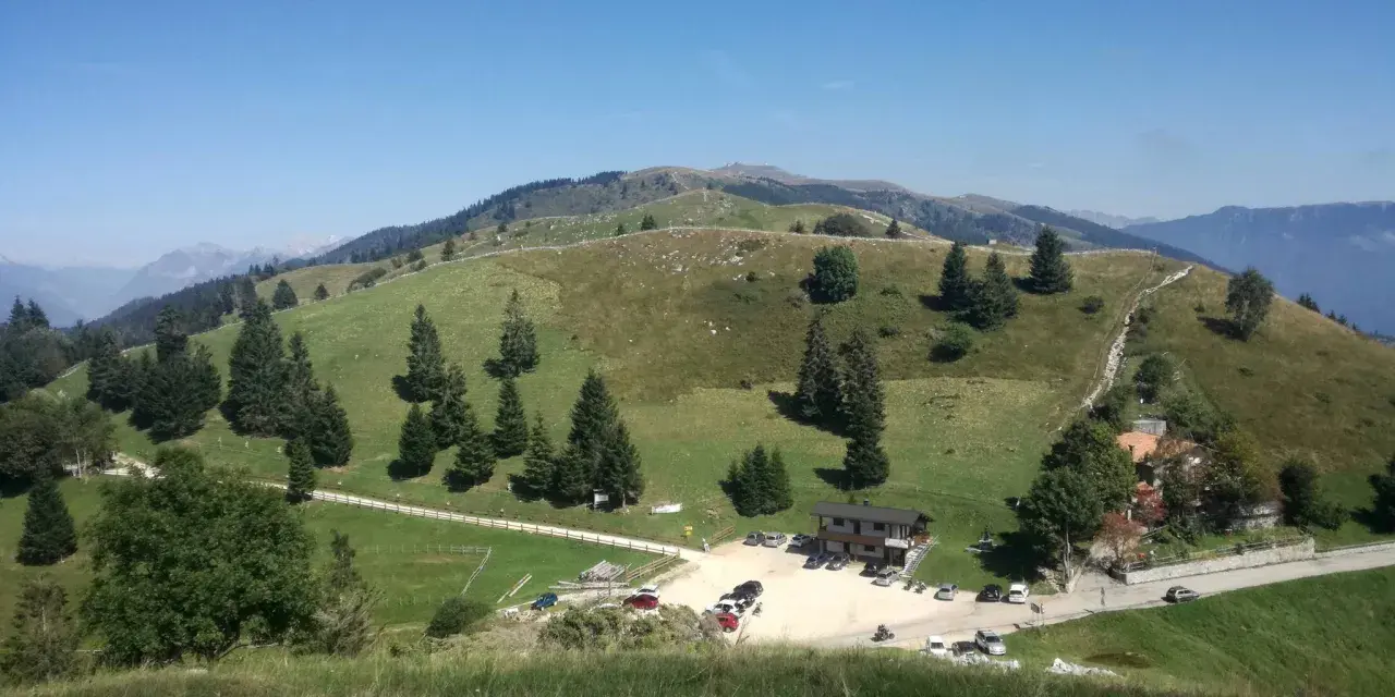 Panorami verdi e dolci colline del Pian delle Femene, con un rifugio e parcheggio.