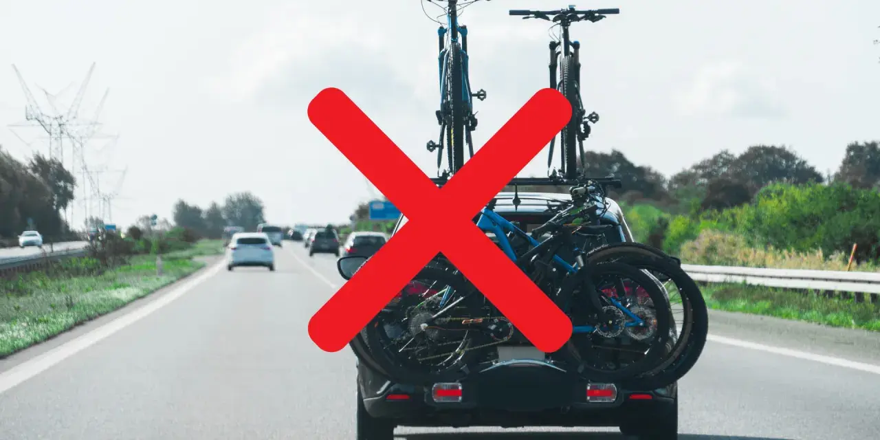 Attenzione al carico sporgente auto! Biciclette sul portabici posteriore, ma una grande X rossa indica un problema di sicurezza.