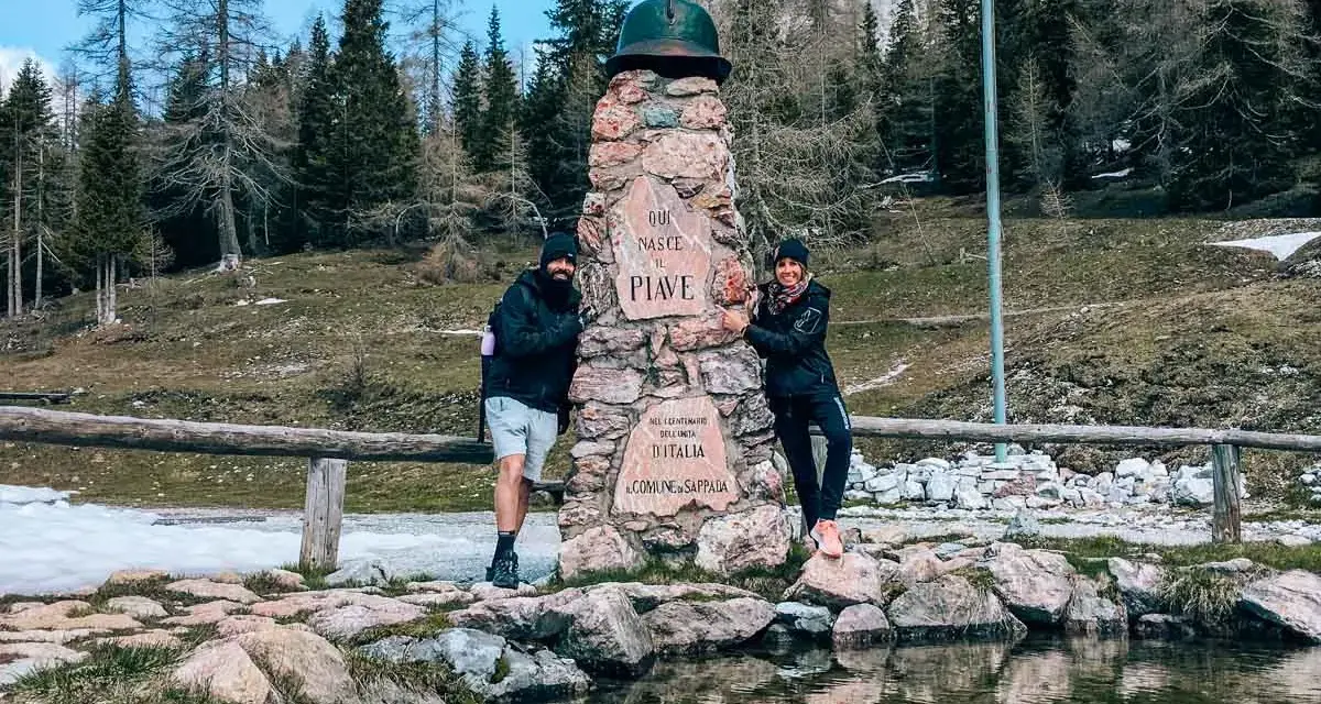 Coppia sorridente vicino a un monumento in pietra a Sappada, ideale per passeggiate facili.