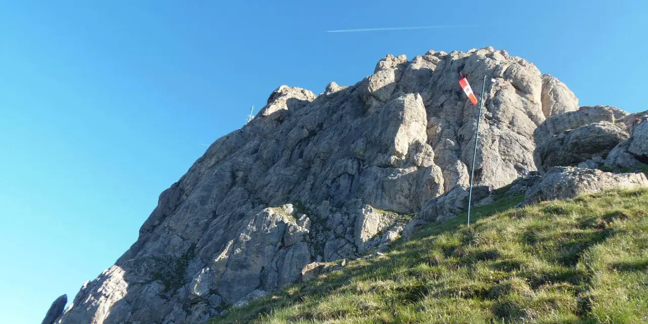 Vetta rocciosa con bandiera segnavento. Per col rodella come arrivare, segui il sentiero erboso verso la cima.