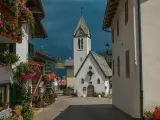 Un pittoresco vicolo a Rocca Pietore, con case fiorite e una chiesa dal cielo tempestoso.