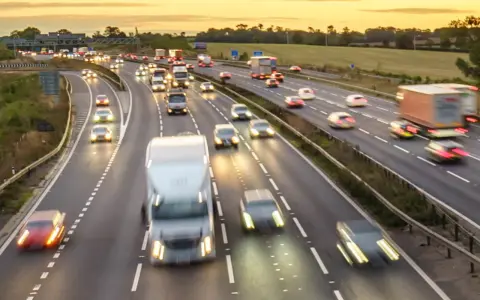 Traffico intenso su un'autostrada al tramonto. Auto e camion sfrecciano, creando scie luminose. Chissà se il limite velocità autostrada 150 dove è rispettato.