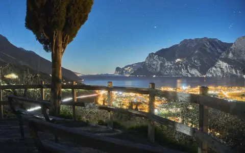 Peschiera del Garda di sera: un panorama mozzafiato con luci scintillanti, montagne imponenti e un cielo stellato. Ideale per una serata romantica.
