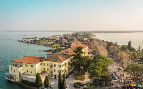 Vista aerea del centro storico di Sirmione, con edifici storici, lago e passeggiata affollata.