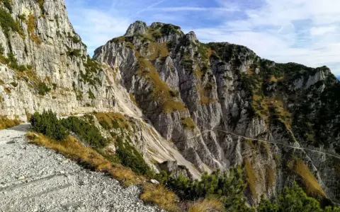 Sentiero roccioso in montagna, parte della strada degli eroi anello, con vegetazione sparsa e cielo azzurro.