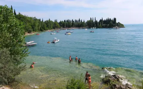 La baia delle Sirene a Garda, con gente che nuota e barche sull'acqua cristallina, sotto un cielo azzurro.