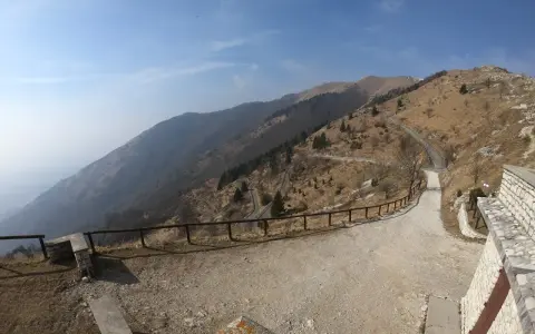 Strada tortuosa sul Monte Palon, Grappa, con vista panoramica sulle montagne e cielo azzurro.