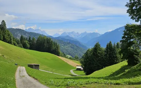 Sentiero tra prati verdi e boschi, con casette di legno e montagne sullo sfondo. Sagron Mis, cosa vedere in questo paradiso alpino!