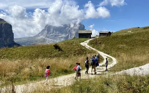 Famiglia in escursione su sentiero facile a Selva di Val Gardena, con baite e montagne sullo sfondo.