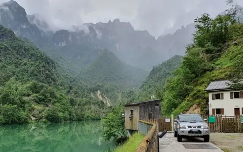 Il lago della Stua, incastonato tra montagne nebbiose e foreste lussureggianti, con una casa e un'auto parcheggiata vicino.