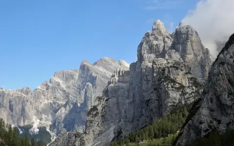 Imponenti cime rocciose dei monti di Framont si stagliano contro un cielo azzurro, con foreste di conifere ai loro piedi.