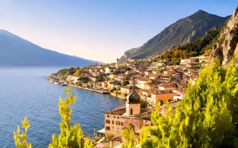 Un perfetto weekend sul lago di Garda: borgo colorato affacciato sull'acqua blu, montagne verdi e cielo limpido.