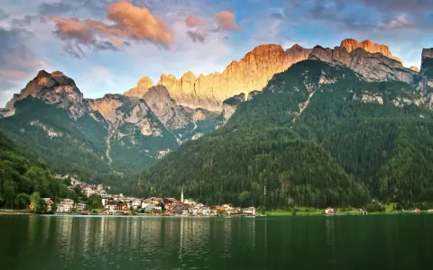 Un incantevole giro del lago di Alleghe, con il paese incastonato tra boschi e montagne maestose illuminate dal sole al tramonto.
