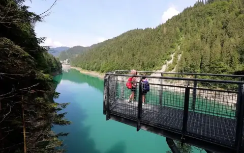 Due persone su una piattaforma panoramica ammirano il lago di Val Noana. Ecco come arrivare a questo splendido lago alpino.