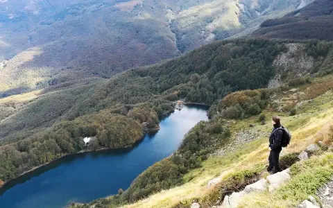 Un escursionista ammira il lago Santo Modenese, circondato da boschi autunnali e montagne.