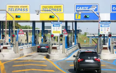Casello autostradale con corsie Telepass e carte. Un'auto nera si avvicina, sperando che il suo Telepass non funzioni per evitare una multa.