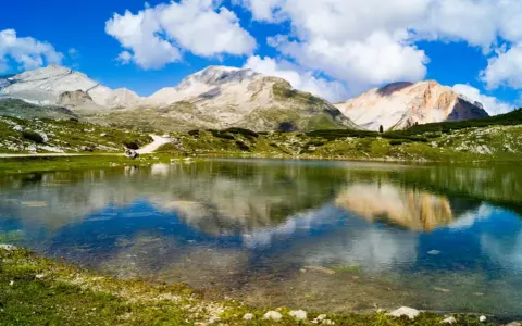 Un limpido lago di limo riflette montagne maestose e un cielo azzurro con nuvole bianche.