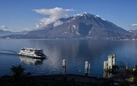 Traghetto sul lago di Como, con montagne innevate sullo sfondo e il pittoresco varenna centro storico.