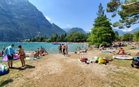 Spiaggia sabbioni Riva del Garda affollata di bagnanti sotto le montagne.