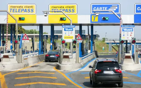 Casello autostradale con auto in coda. Segnaletica per Telepass e carte di credito. Possibile problema di mancato pagamento Telepass per un veicolo.