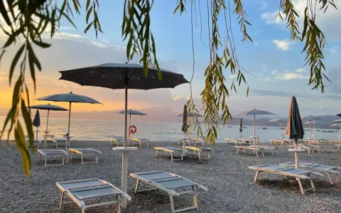 Alba sul lago di Garda, con lettini e ombrelloni pronti per accogliere i bagnanti sulle sue spiagge di sabbia.